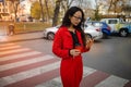 Asian woman with smartphone walking against city street.  Fashion business photo of beautiful girl in red suit with smart phone an Royalty Free Stock Photo