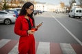 Asian woman with smartphone walking against city street.  Fashion business photo of beautiful girl in red suit with smart phone an Royalty Free Stock Photo