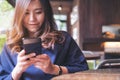 Asian woman with smiley face using and looking at a black smart phone in modern loft cafe Royalty Free Stock Photo