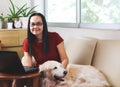 Woman smiling and looki to camera , sitting on couch in living room with computer in front of her and golden retriever dog lying