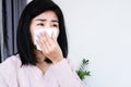 Asian woman sneezing, coughing allergic rhinitis to the bad weather hand holding paper tissue covering her runny nose