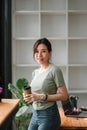 Asian woman standing on front of office workplace while hand holding a cup of coffee and looking outside Royalty Free Stock Photo