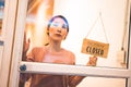 Asian woman store owner turning hanging closed sign in front door