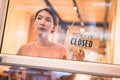 Asian woman store owner turning hanging closed sign in front door