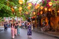 Hoi An, Vietnam. Asian dressed women stroll through an avenue in the tourist attraction, in whose trees hang illuminated lanterns Royalty Free Stock Photo