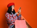 Asian woman in a stylish beret and sweater, with a colorful shopping bag looks into her mobile phone and something is surprised Royalty Free Stock Photo