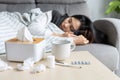 Asian woman suffering from covid-19 symptoms have to be on self-isolation at home. Girl has a fever lying on couch with tissue,