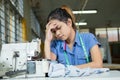 Asian woman tailor holds her head because she hurts while sewing clothes