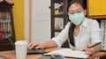 Asian woman is taking notes and using a laptop. She works at home to protect against the Corona virus or Covid-19 Royalty Free Stock Photo