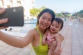 Asian woman taking selfie photo with her adorable baby girl - beautiful Chinese mother holding her little daughter and taking Royalty Free Stock Photo