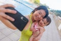 Asian woman taking selfie photo with her adorable baby girl - beautiful Chinese mother holding her little daughter and taking Royalty Free Stock Photo