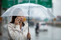 Asian woman talking on cell phone and holding umbrella while standing on the city street in the rainy day Royalty Free Stock Photo