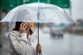 Asian woman talking on a cell phone and holding umbrella while standing on the city street in rainy day Royalty Free Stock Photo