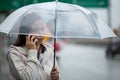 Asian woman talking on cell phone and holding umbrella while standing on the city street in the rainy day Royalty Free Stock Photo