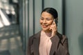 Asian woman talking on a mobile phone in the street. Businesswoman in jacket holds phone at ear and smiles. High quality