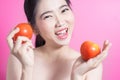 Asian woman with tomato concept. She smiling and holding tomato. Beauty face and natural makeup. Isolated over pink background.