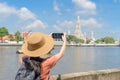 Asian woman, a tourist people, travelling, taking a photo with smartphone in Temple of Dawn or Wat Arun and Chao Phraya River,