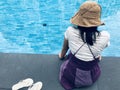 Asian woman tourist sit back and soak her legs in the water wearing the  woven hat sit by the blue swimming pool side and take Royalty Free Stock Photo