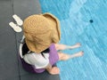 Asian woman tourist sit back and soak her legs in the water wearing the woven hat sit by the blue swimming pool side and take