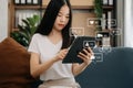 Asian woman typing smartphone, keyboard with laptop computer of Social media and Marketing virtual icons screen concept. on sofa Royalty Free Stock Photo