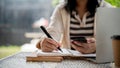 An Asian woman using her smartphone and taking notes on her notebook at a table in a coffee shop Royalty Free Stock Photo