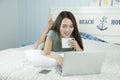 Asian woman using laptop and drinking coffee while lying on her bed. Royalty Free Stock Photo