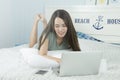 Asian woman using laptop and see the message on smartphone while lying on her bed. Royalty Free Stock Photo