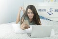 Asian woman using laptop and smartphone while lying on her bed. Royalty Free Stock Photo