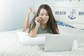 Asian woman using laptop and speak on phone while lying on her bed. Royalty Free Stock Photo