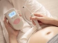 Asian woman using pocket fetal doppler to monitor baby heart beat. expectant mother happy and smile when examine belly. Royalty Free Stock Photo