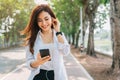 Asian woman using the small talk headphones to make a happy phone call in the park Royalty Free Stock Photo