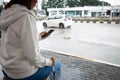 Asian woman is using on smartphone, checking social media network while waiting taxi at bus stop in rainy day