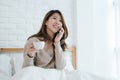 Asian woman using the smartphone on her bed while holding cup of coffee in the morning. Royalty Free Stock Photo