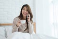 Asian woman using the smartphone on her bed while holding cup of coffee in the morning. Royalty Free Stock Photo