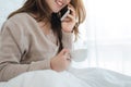 Asian woman using the smartphone on her bed while holding cup of coffee in the morning. Royalty Free Stock Photo
