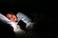 Asian woman using smartphone at night on the bed in dark room, Using smartphone in dark may be causes of eye pain symptom,Health Royalty Free Stock Photo