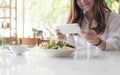 An asian woman using smartphone to taking photo of salad in a white plate on table in cafe