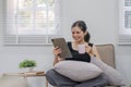 Asian woman using tablet watching video sitting on sofa in living room at home. Happy young Asian woman relaxing at home Royalty Free Stock Photo