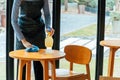 Asian woman waitress staff in apron cleaning table with disinfectant spray for protect infection coronavirus covid-19 in cafe Royalty Free Stock Photo