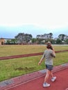 An asian woman is walking on the track of a school, and talking on the phone while walking.