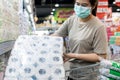 Asian woman wear face mask,chooses tissue paper,toilet paper while shopping food,people panic buying, hoarding during the Covid-19