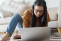 Asian woman wear glasses and casual suite  is working on laptop.Women sitting on the floor with a sofa in the back her in the Royalty Free Stock Photo