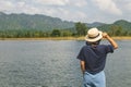 Asian woman wear hat and standing relax on green grass meadow field, she looking forward to lake and mountain. Royalty Free Stock Photo