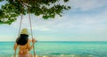 Asian woman wear swimwear and hat swing the swings at sand beach and looking beautiful tropical paradise sea and sky on sunny day Royalty Free Stock Photo