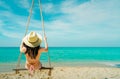 Asian woman wear swimwear and hat swing the swings at sand beach and looking beautiful tropical paradise sea and sky on sunny day Royalty Free Stock Photo