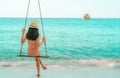 Asian woman wear swimwear and hat swing the swings at sand beach and looking beautiful tropical paradise sea and sky on sunny day Royalty Free Stock Photo