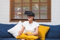 Asian woman wear vr headset glasses and play virtural reality sitting on sofa at home.digital tehcnology lifestyle