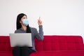 Asian woman wearing a face mask and using a laptop on the sofa for working from home and Pointed to the top. New lifestyle normal