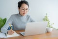 Asian woman wearing glasses is using laptop at home office.Portrait young cute student working on smart technology gadget Royalty Free Stock Photo