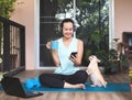 Asian woman wearing headphones, holding coffee cup, using smartphone, sitting  on yoga mat in balcony  with computer laptop Royalty Free Stock Photo